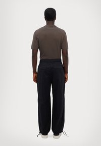 Camisa de manga curta castanha escura, calças cargo largas de cor azul marinho com cintura elástica, bainhas ajustadas e ténis brancos.
