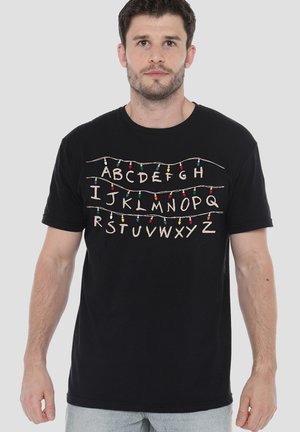 Mann trägt schwarzes T-Shirt mit den Buchstaben A bis Z, die durch bunte Lichterketten über der Brust verbunden sind.
