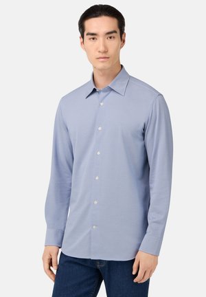 Light blue long-sleeve button-up shirt made of smooth fabric, featuring a standard collar and pearlized buttons, worn with dark jeans.