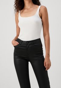 Vit ribbad linne med fyrkantig halsringning, kombinerat med högmidjade svarta fusk läderbyxor med en slät, glänsande yta.