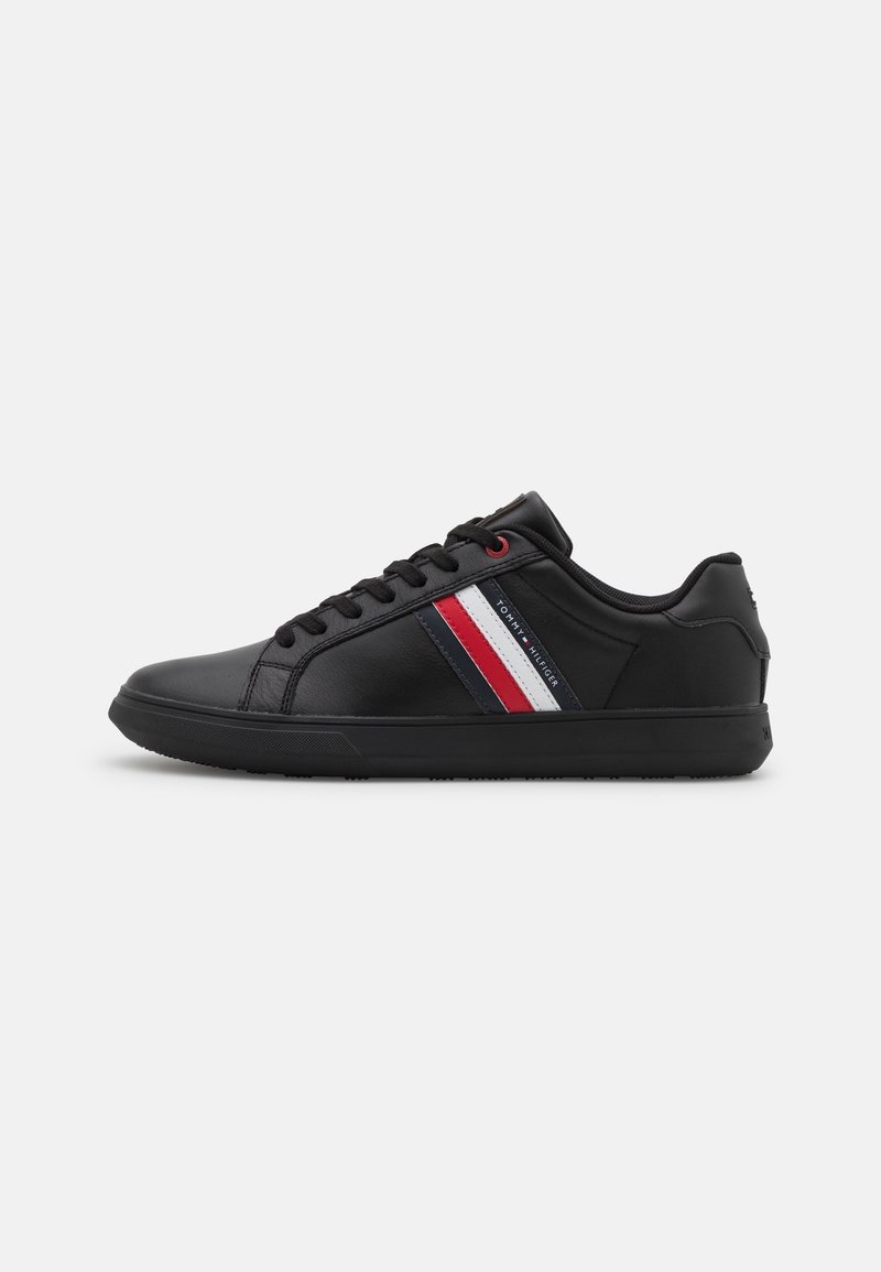 Baskets basses noires avec des lacets noirs, une semelle noire et des bandes rouges, blanches et bleues sur le côté avec le texte "Tommy Hilfiger".