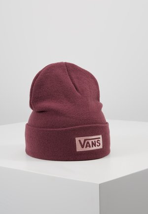 Bonnet tricoté marron avec un revers plié présentant un patch logo Vans rose, exposé sur un socle blanc sur fond gris.