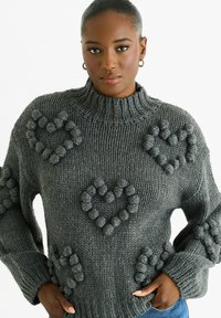 Gray chunky knit sweater with a high neck, featuring plush heart patterns. Loose fit with textured accents on sleeves and body.