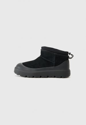 Bottes chelsea en daim noir avec un bout rond, semelle en caoutchouc texturée et une tirette à l'arrière. Présente un design ajusté avec un revers.
