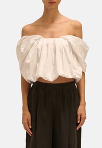 Biała bluzka z odkrytymi ramionami, z marszczonym materiałem i skróconym krojem, w połączeniu z luźnymi, ciemnoszarymi spodniami z elastycznym paskiem.