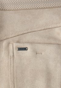 Beige suède stof met zichtbare stiksels, een gestructureerde geweven band en een klein metalen label met de tekst "Street One" bevestigd nabij de rand van een zak.