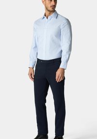 Lichtblauw gestreept overhemd met een puntige kraag, knopenlijst aan de voorkant en lange mouwen, gecombineerd met marineblauwe broek en zwarte schoenen.