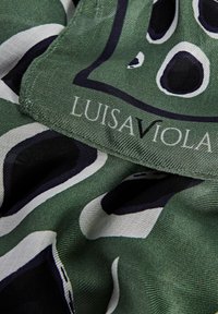 Bufanda de seda verde con un patrón ondulado en blanco y negro. Cuenta con una etiqueta cosida con el texto "LUISA VIOLA" en blanco. Textura suave.