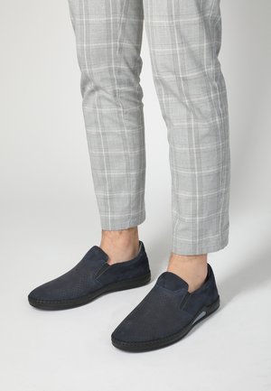 Mørkeblå ruskind slip-on sko med perforeret overdelsdesign, sort ydersåle og kontrasterende syninger. Båret med gråternet cropped-bukser.