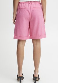 Vaaleanpunaiset polvipituiset shortsit, jotka on valmistettu sileästä, teksturoidusta kankaasta. Lyhyt lahje on käännetty, ja takana on kaksi taskua. Rento vyötärönauha, joka tarjoaa säädettävän istuvuuden.