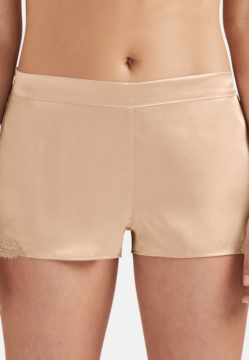 Shorts beiges en tissu lisse, avec un détail en dentelle à l'ourlet sur un côté. Le design est ajusté avec une taille simple.