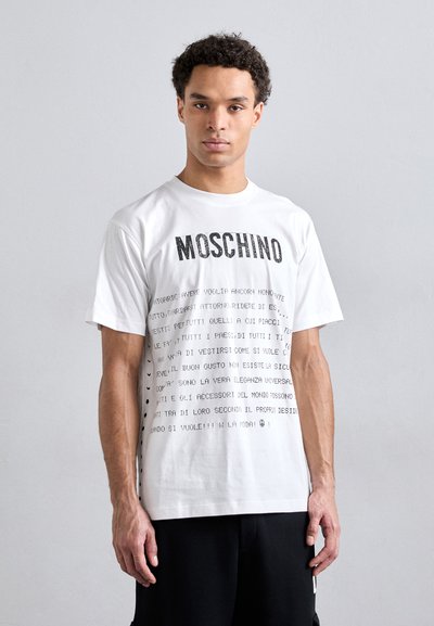 T-shirt alb din bumbac, având logo-ul "Moschino" în litere negre îndrăznețe, cu text și grafice imprimate răspândite pe întreaga țesătură.