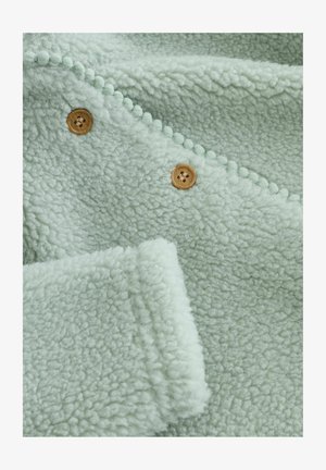 Džemperasta tkanina u meko zeleni boji s teksturiranom površinom, zaobljenim akcentima i dva drvena dugmeta za zatvaranje.