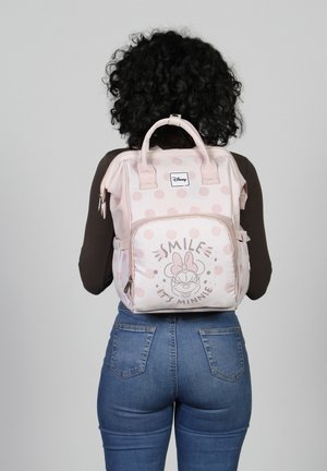 Lichtroze rugzak met witte stippen, voorzien van een voorzak met rits waarop een Minnie Mouse-afbeelding staat met de tekst "LACH, HET IS MINNIE."
