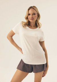 White cotton t-shirt with a round neckline and short sleeves, paired with dark purple polka dot shorts. Text on the shirt reads "Can't wait for Sundays."