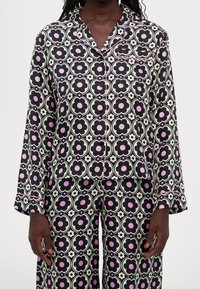 Ensemble de pyjama noir et blanc avec des motifs floraux roses, comprenant un haut boutonné à manches longues et un pantalon assorti.