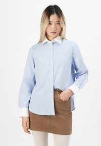 Light blue, long-sleeved shirt with white collar and vertical stripes, paired with a brown skirt. Features button closure and a chest pocket.