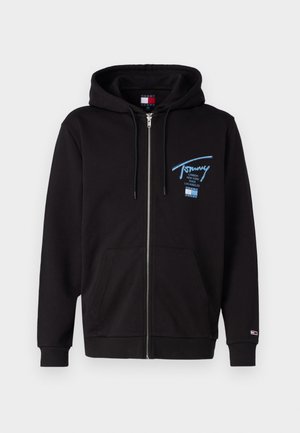 Svart hettegenser med glidelås laget av bomull, med en frontlomme, snøring i hetta og blå brodert logo på venstre bryst.
