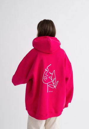 Roze hoodie met een grote, wit lijngetekende gezichtsgrafiek op de achterkant. Beschikt over een ruime capuchon en een ontspannen pasvorm. Zachte stoftextuur.