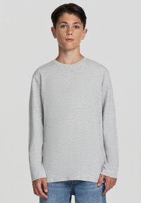 Jasnoszary, długi rękaw, koszulka z okrągłym dekoltem, wykonana z miękkiego materiału, charakteryzująca się strukturalnym wykończeniem i luźnym krojem. Połączona z niebieskimi dżinsami.