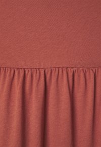 Tissu brun rougeâtre, texturé, avec une partie supérieure lisse et une partie inférieure froncée, créant un design fluide et en niveaux.