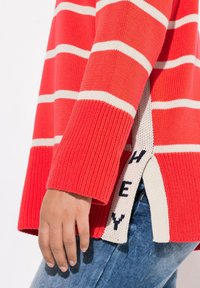 Sweter w czerwono-kremowe paski, z prążkowaną fakturą, bocznymi rozcięciami oraz dzianinowym akcentem z napisem "HEY" na dolnym brzegu.