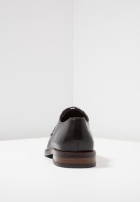 Chaussure en cuir noir avec un bout arrondi, un profil bas et un talon en bois. Présente une texture lisse et un design minimaliste.