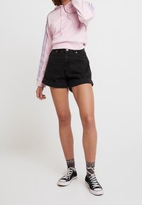 Mustat farkkushortsit, joissa rullatut lahkeet, yhdistetty vaaleanpunaiseen collegepaitaan, jossa siniset raidat hihoissa ja nyörisomisteinen huppu. Mustat lenkkarit.