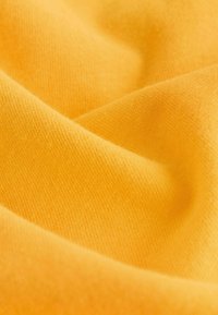 Geel katoenen stof met een gladde textuur, met fijne, gelijkmatige brei en subtiele warmte in kleur, die zachte, gedrapeerde plooien toont.