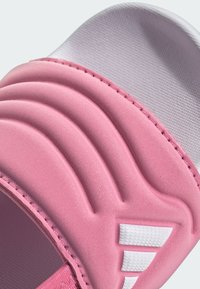 Růžový pěnový polstrovaný popruh sandálu se třemi texturovanými bílými šikmými pruhy na světle šedé texturované podešvi.