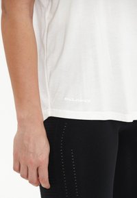 Vit t-shirt med kort ärm med "ENDURANCE"-logotyp i reflekterande tryck vid fållen, i kombination med svarta leggings med strukturerade sidopaneler.