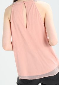 Rose cotton tank top with a keyhole back, textured surface, and beaded accents on the shoulders. Relaxed fit, hem falls below the waist.