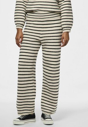 Ensemble de détente en tricot rayé crème avec des rayures noires et vertes, comprenant un pantalon large et un pull court. Chaussettes et baskets visibles.