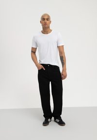 Witte crew-neck t-shirt, zwarte broek en zwarte sportschoenen. De broek heeft een rechte snit en een enkele knoopsluiting. Glad materiaal.
