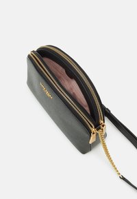 Svart och grå syntetisk materialväska med guldzipper, kedjedetalj och rosa innervägg. Har dubbla fack och en smal design.