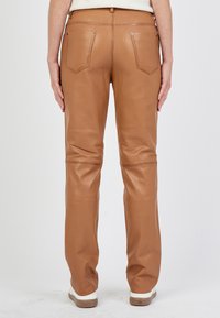 Tan leren broek met een aansluitend ontwerp, voorzien van twee achterzakken en subtiele stikseldetails. Het materiaal heeft een gladde textuur.