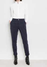 Navy blue cotton trousers with a relaxed fit, featuring front pockets and a cuffed hem, paired with a white button-up shirt. Black ankle boots.