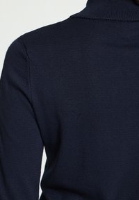 Pull à col roulé en maille bleu marine montrant l'épaule et la partie supérieure du dos.