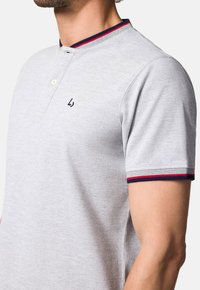 Szary polo z dwuknopkowym zapięciem, krótkimi rękawami i kołnierzykiem w niebieskie i czerwone paski. Zawieża subtelne haftowane logo na piersi.