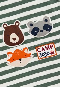 Žalias ir baltas dryžuotas audinys, kuriame esantys trys gyvūnų aplikacijos: rudas lokys, pilkas oposumas ir oranžinė lapė, su „CAMP Jojo“ pleistru.