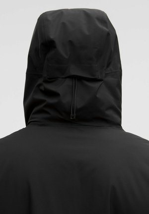 Fekete vízálló dzseki állítható kapucnival, hátulról nézve, világos egyszínű háttéren.