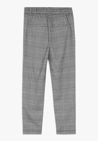 Šedé kostkované kalhoty s elastickým pásem, které mají kombinaci velkých a malých kostkovaných vzorů a dvě zadní kapsy.