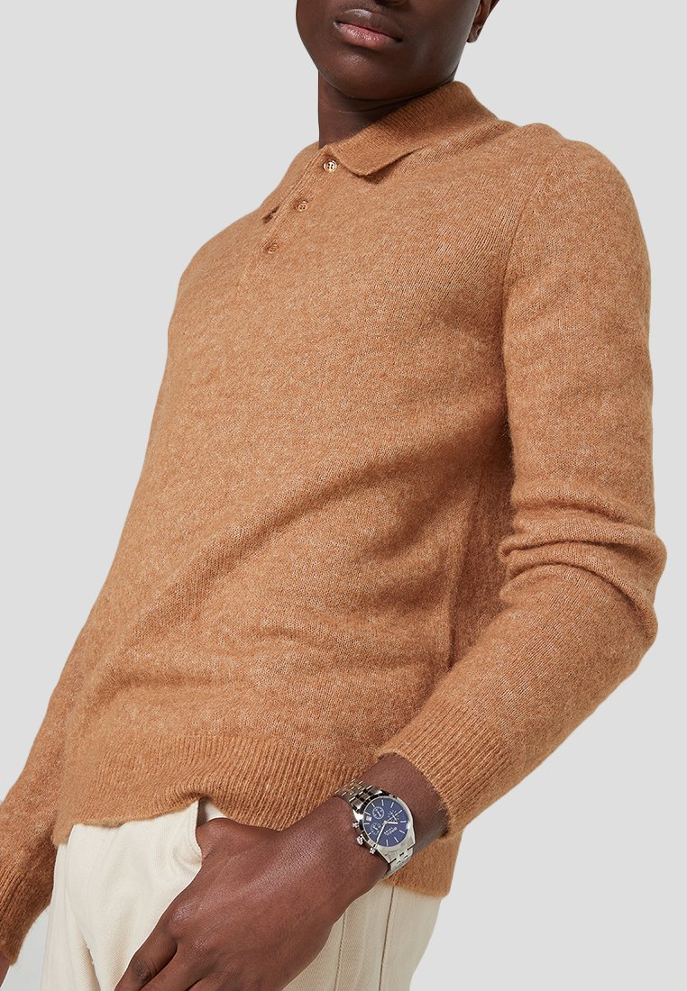 Pulóver de mezcla de lana marrón con cuello tipo polo, que presenta un corte ajustado, puños acanalados y una textura suave. Lleva un reloj en la muñeca.