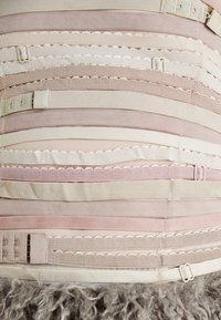 Geflochtene Textilschichten in sanften rosa und beigen Tönen, mit verschiedenen Breiten und Texturen, versehen mit hardware Clips und gewellten Kanten.