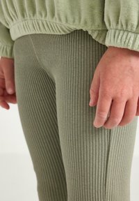 Vihreät ribattu leggingsit, jotka on valmistettu tekstuurikankaasta, yhdistettynä saman sävyiseen kerättyyn neulepaitaan, jossa on joustavat hihansuut ja rento istuvuus.