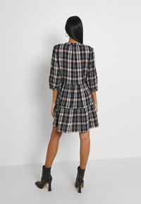 Musta ja beige ruudullinen lyhyt mekko, jossa on puffattuja hihoja, kerroksellinen hame ja kerätty selkäosa. Viety mustilla nilkkasaappailla.