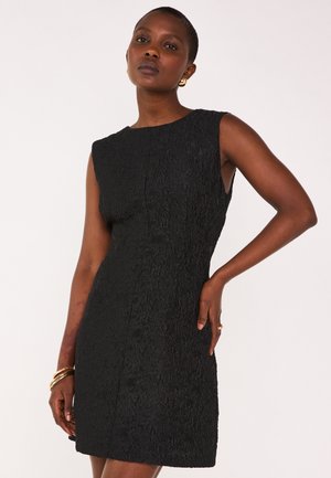 Robe noire sans manches en tissu texturé, de forme ajustée et à ourlet mi-genou. Présente un motif subtil et un col rond.