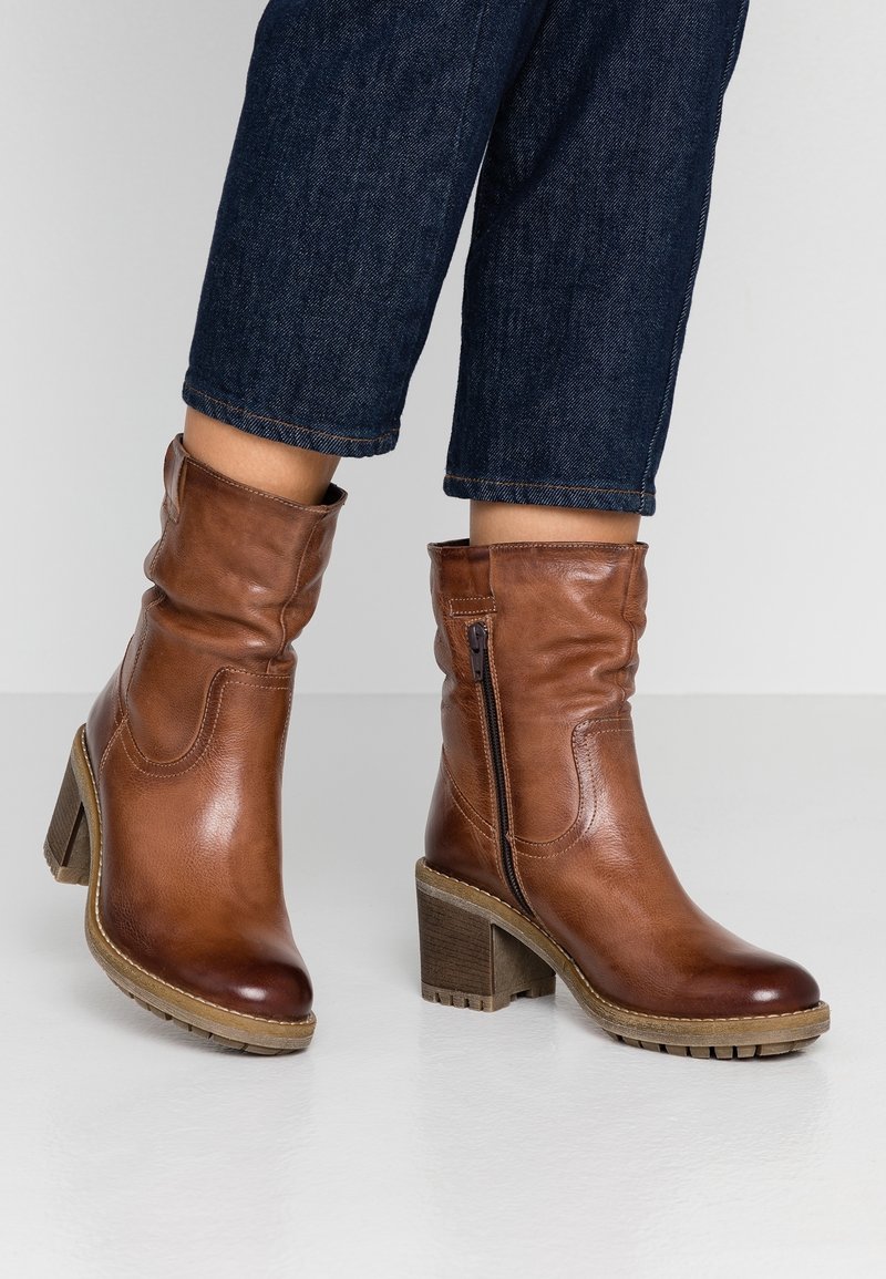 Bottes à cheville en cuir marron au design décontracté, fermeture éclair latérale et talon en bois épais. Semelle en caoutchouc avec motif texturé.