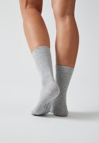 Graue gerippte Socken mit weicher Textur und mittellanger Länge, mit verstärktem Fersen- und Zehenbereich, vor einem weißen Hintergrund präsentiert.