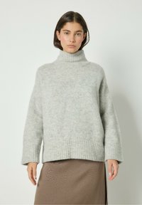 Maglione grigio chiaro a maglia spessa con colletto alto, polsini e orlo a costine. Tessuto morbido, spalle scese e vestibilità aderente.